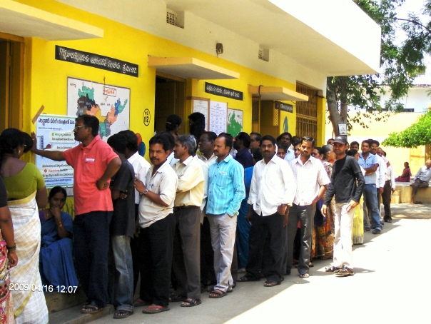 At the Kakaguda Government Primary School in Picket, Secunderabad, Andhra Pradesh, people waited in long lines this afternoon, framed by the bright yellow walls to enter classrooms converted into poll booths.